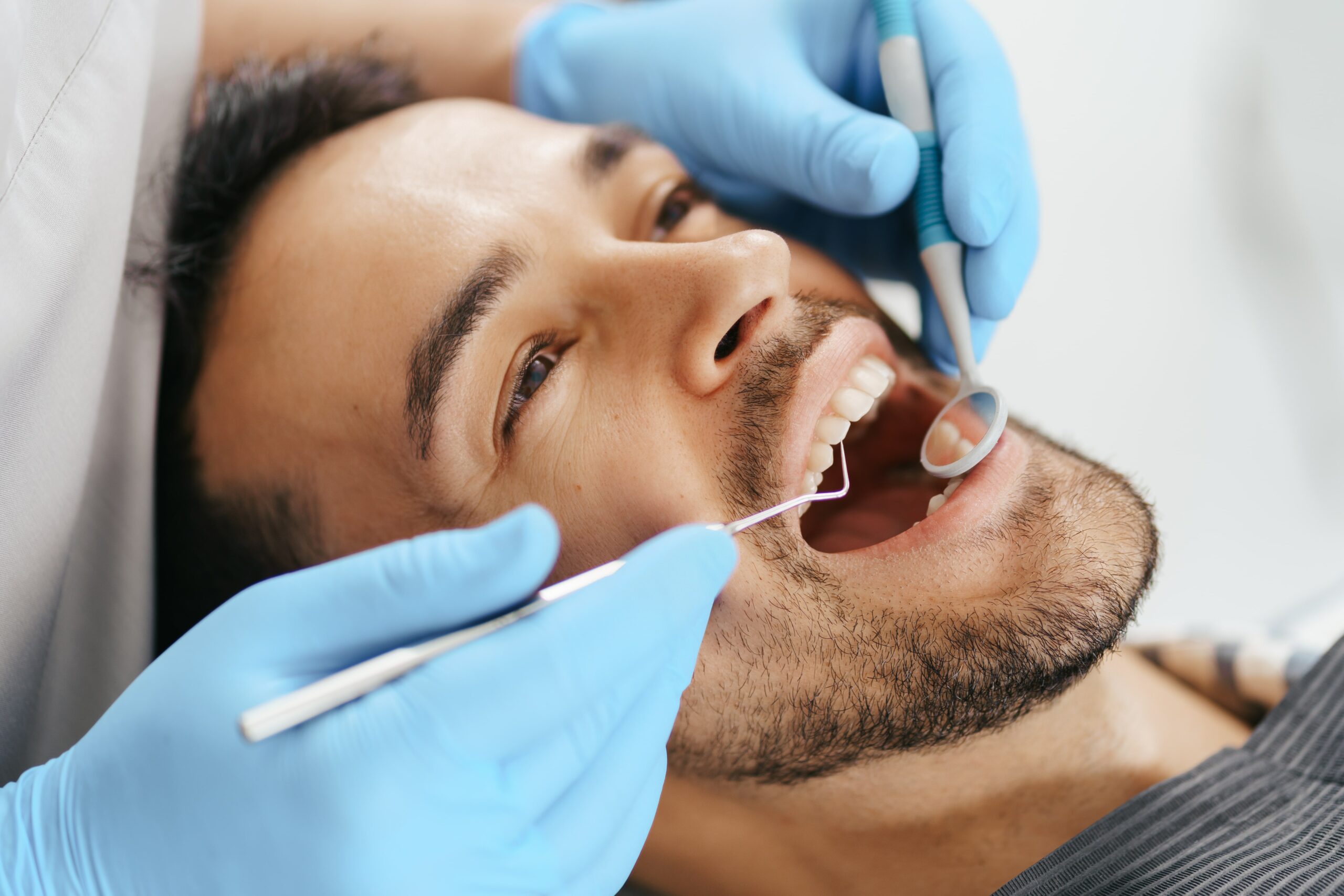 Smiling young man sitting in dentist chair while doctor examining his teeth min scaled 1